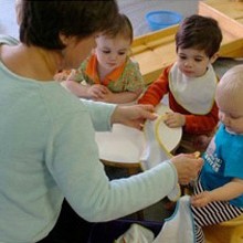 RIE® Associate Ruth Anne Hammond offering a bib to a toddler during snack time at a RIE Parent Infant Guidance™ Class 