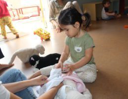 Toddler putting clothes on a doll with the help of her mom at a RIE Parent Infant Guidance Class at the RIE Center in Hollywood.