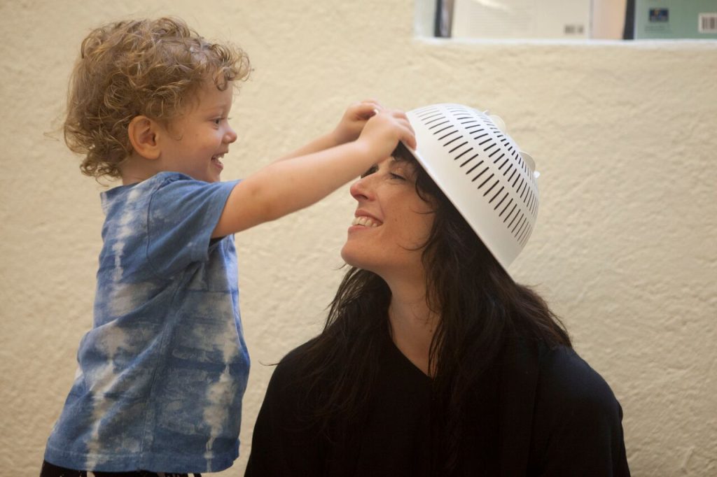 Toddler smiles as he places at colander on his mom's head at RIE® Parent-Infant Guidance™ Classes at RIE Hollywood Center
