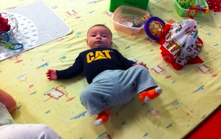 Infant on their back in a colorful play space looking intently at the camera.