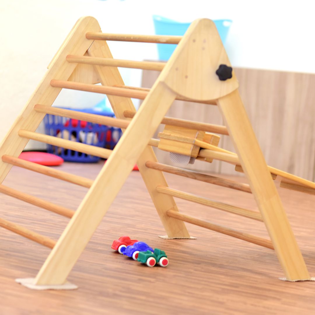 Pikler® Triangle with three plastic toy cars underneath it.
