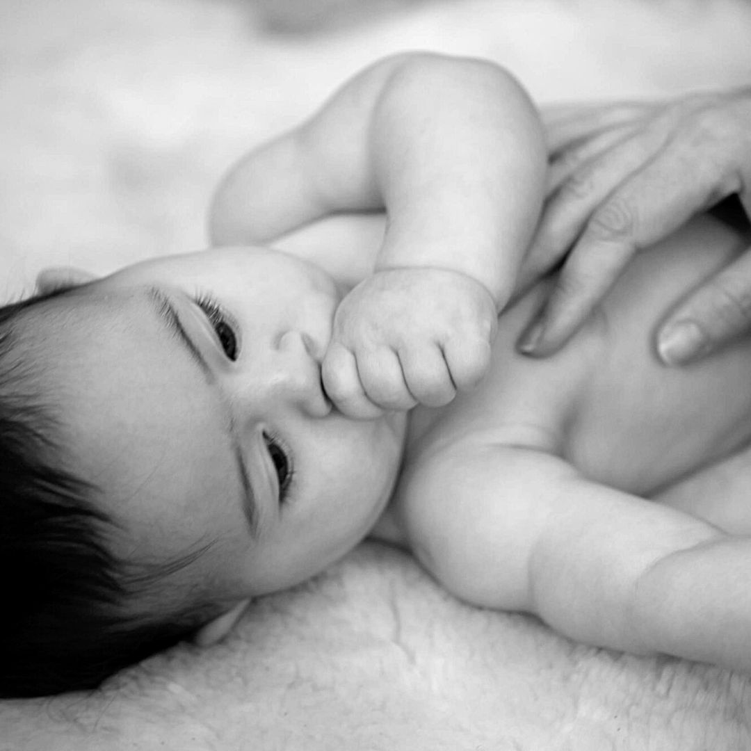 BW photo of a baby lying on their back sucking thumb and looking peacefully at parent