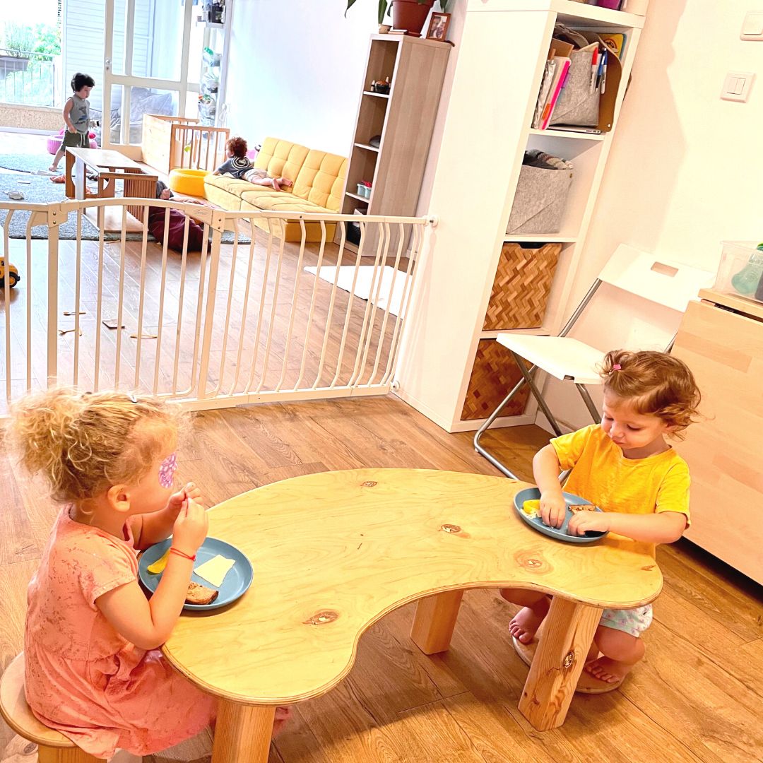 Two toddlers at low table eating lunch together in a childcare setting.